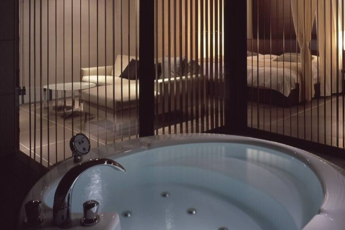 Un área de spa con una bañera grande, un sofá y una cama visibles a través de una ventana.