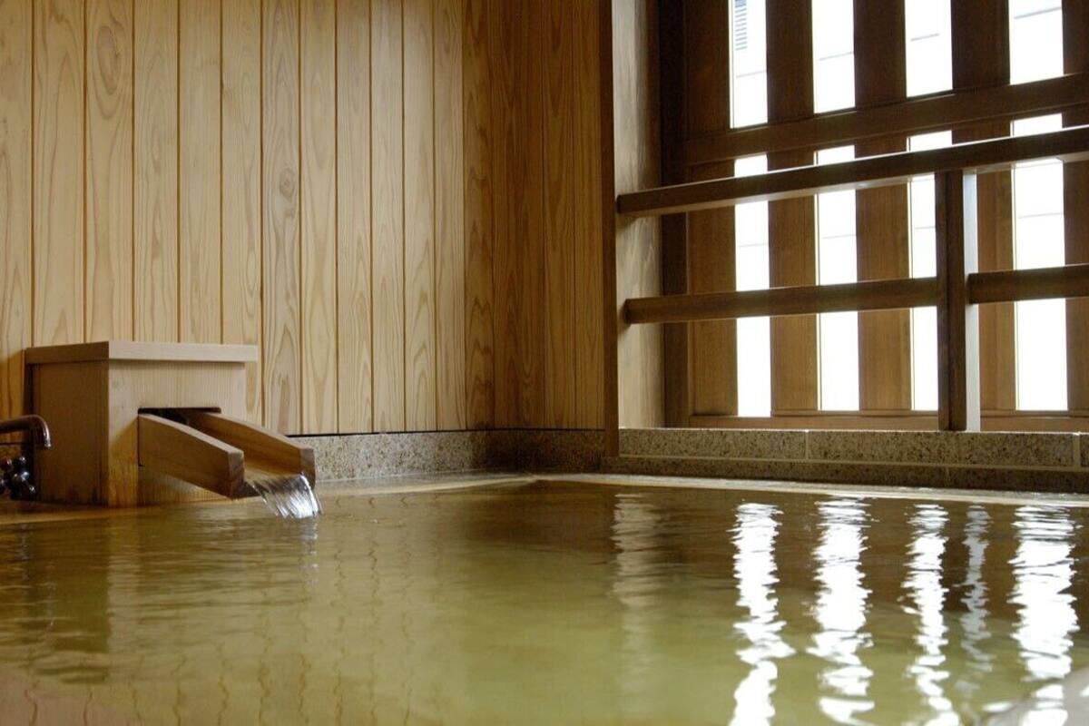Un interior de madera con una gran piscina cubierta, un banco de madera y un ventanal con persianas verticales.