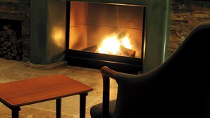 A fireplace with a stone surround, a wooden table, and a black chair in a room with a plain wall.