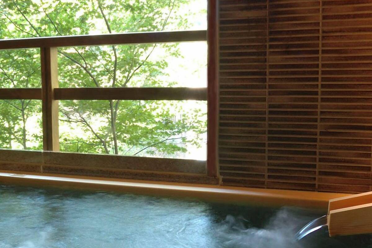 Un jacuzzi con vapor saliendo, una ventana con persianas y árboles a la vista.