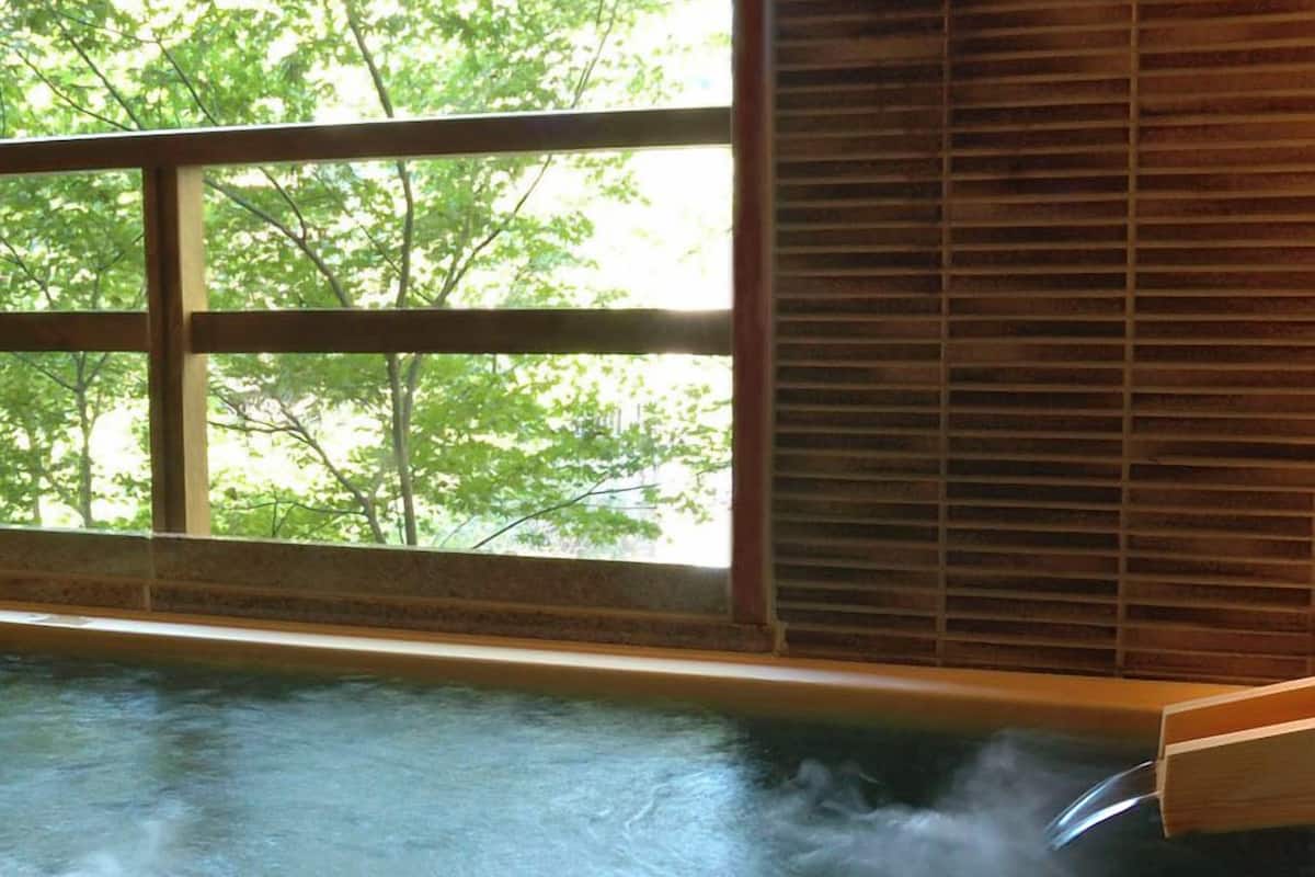 A hot tub with steam rising, a window with blinds, and trees visible outside.