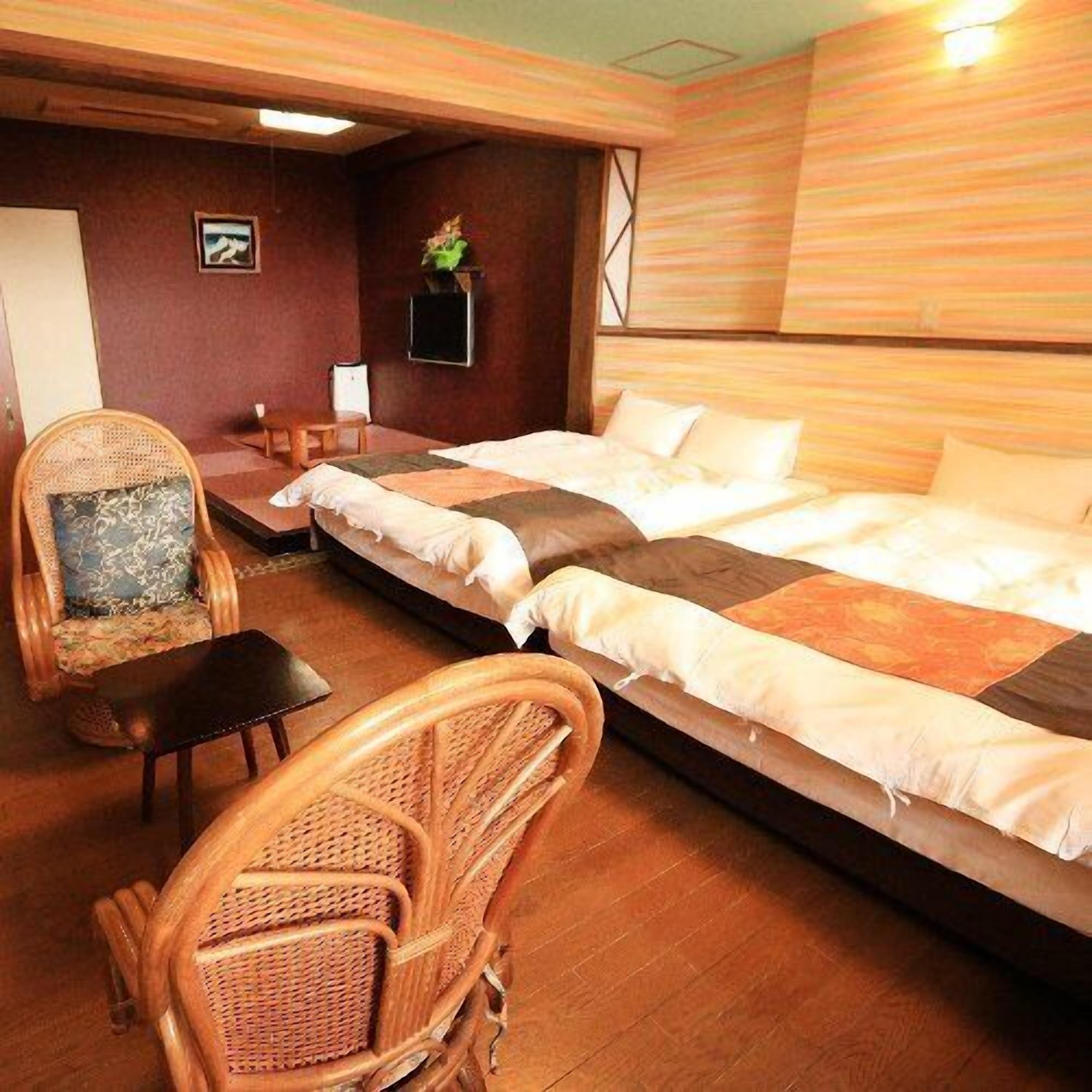 A room with a bed, two chairs, a small table, and a wall-mounted TV.