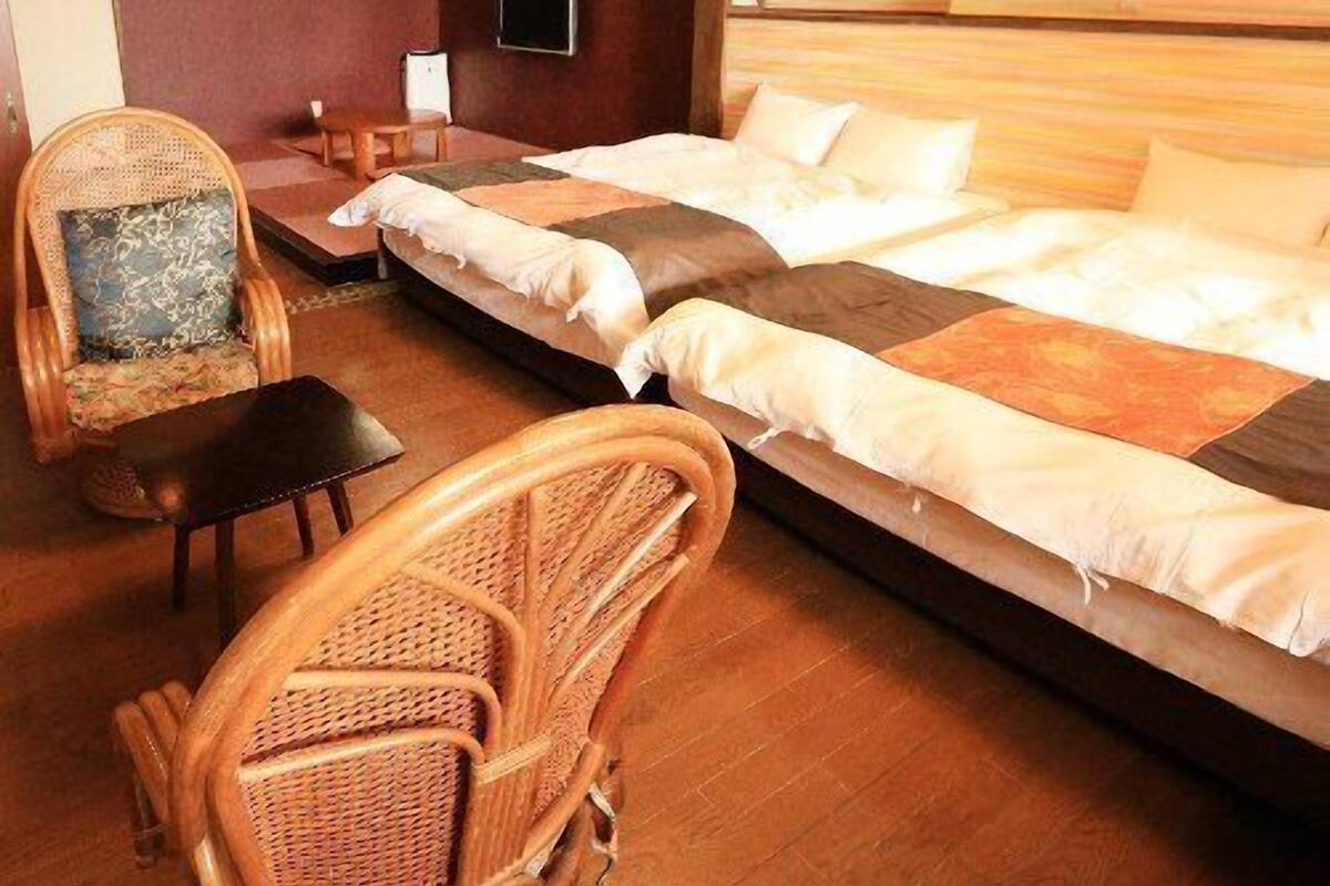 A room with a bed, two chairs, a small table, and a wall-mounted TV.