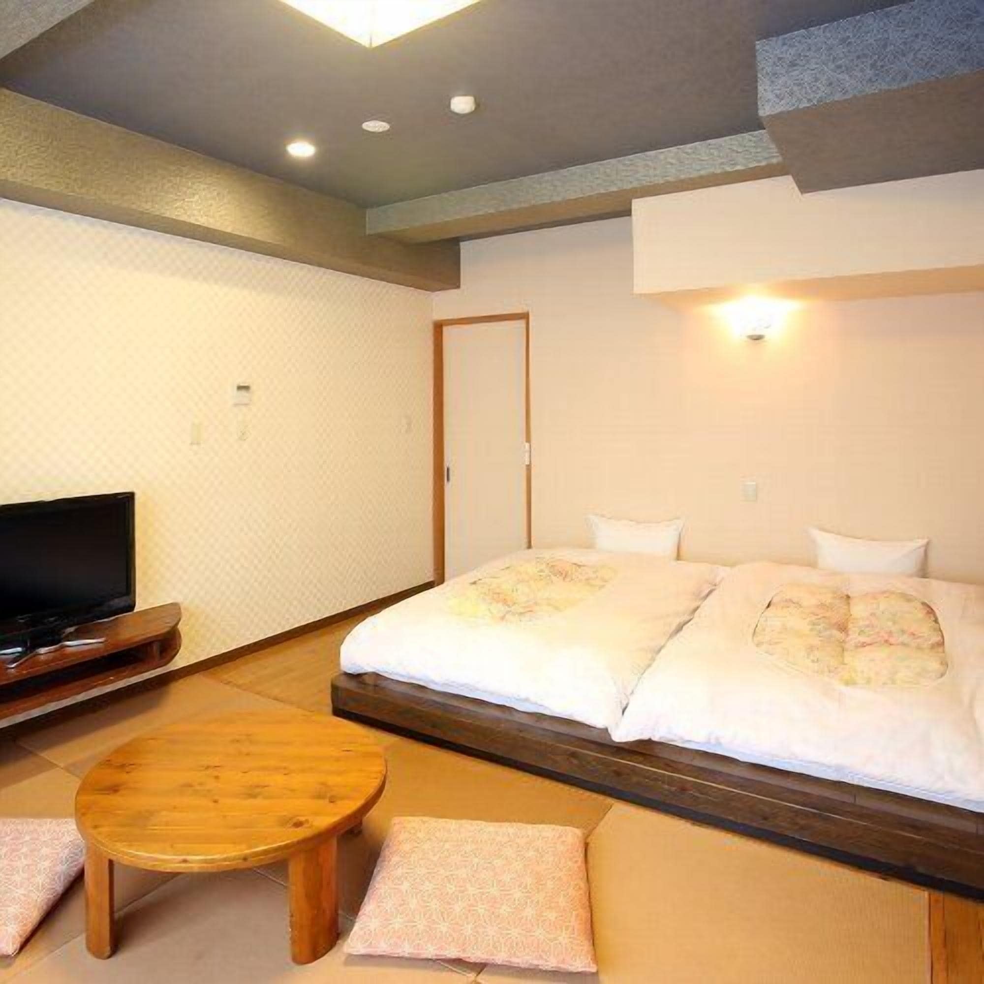 A hotel room with a bed, a television, a wooden table, and a small seating area.