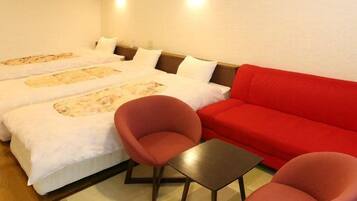 A hotel room with two beds, a red sofa, two red chairs, and a small table.