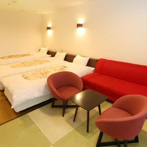 A hotel room with two beds, a red sofa, two red chairs, and a small table. - Asouchinomaki Onsen Yumeoiso (Aso)
