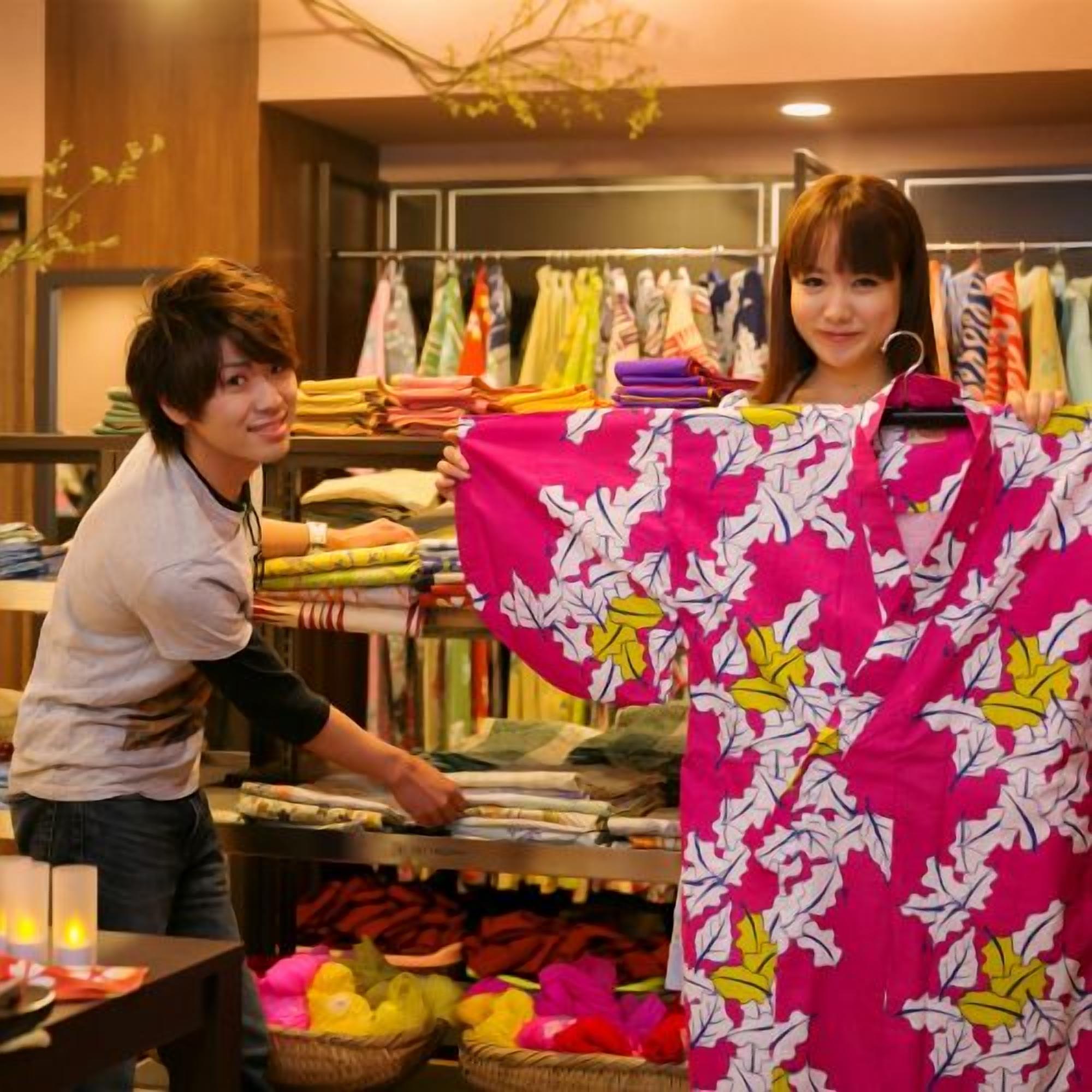 A person holding a colorful garment in a retail setting with clothing racks in the background.