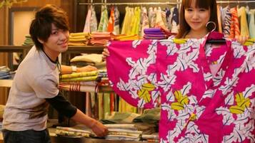 A person holding a colorful garment in a retail setting with clothing racks in the background.