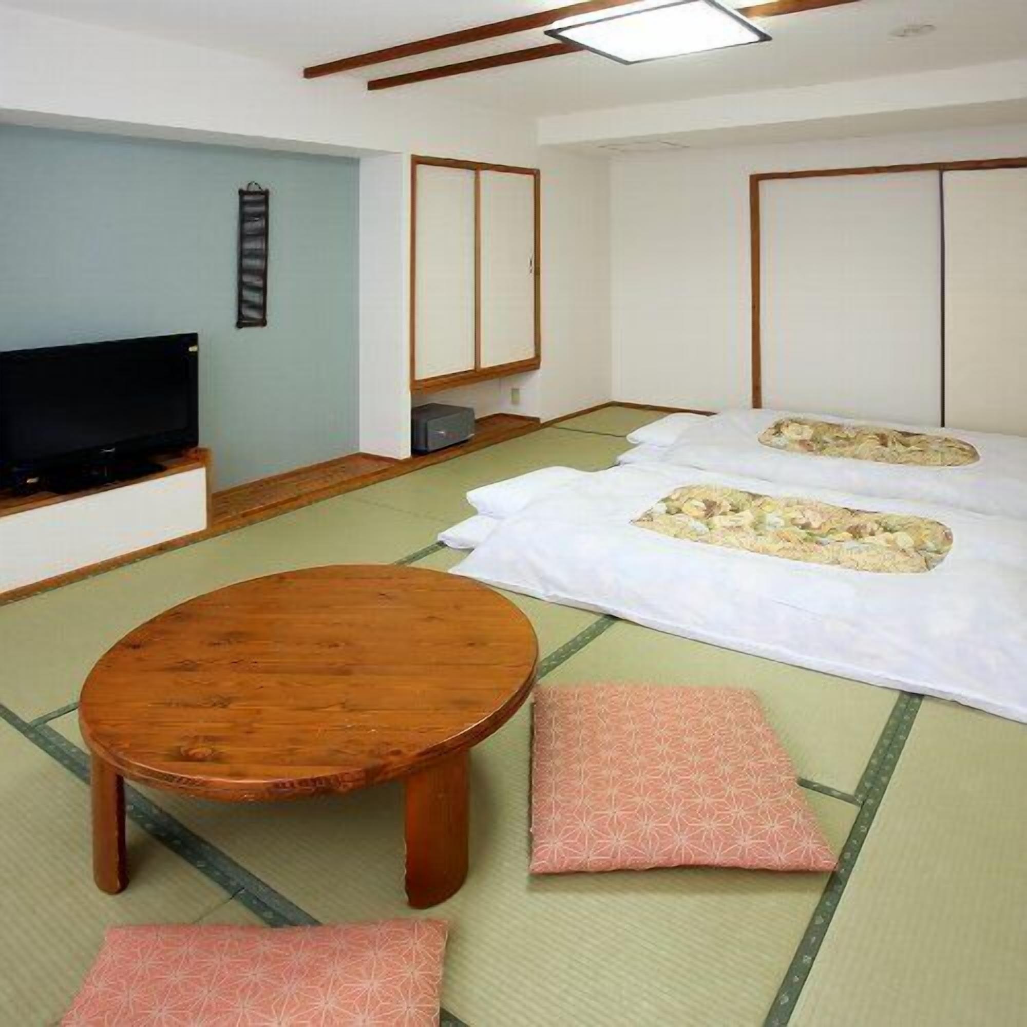 A traditional Japanese-style room with tatami flooring, a television, a wooden table, and futon beds.
