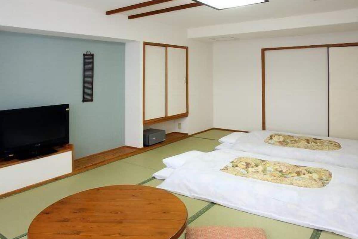 A traditional Japanese-style room with tatami flooring, a television, a wooden table, and futon beds.