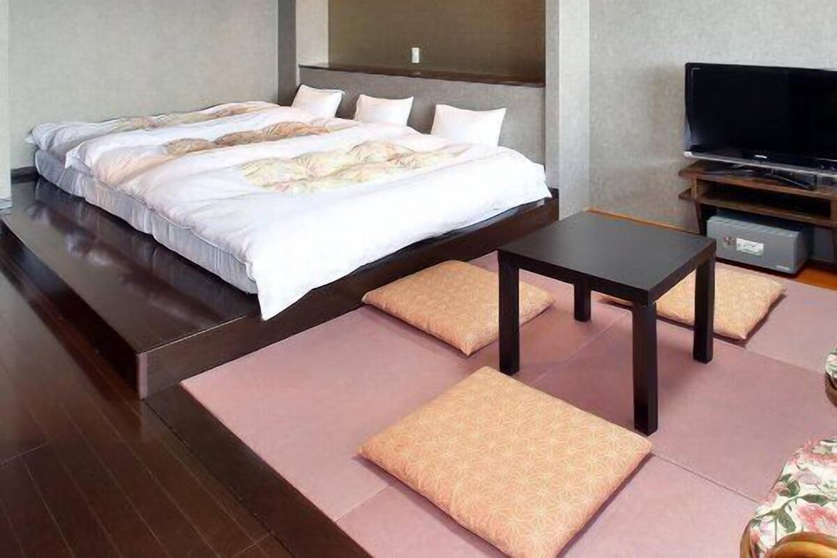 A modern hotel room with a large bed, a flat-screen TV, a small table, and a sofa.