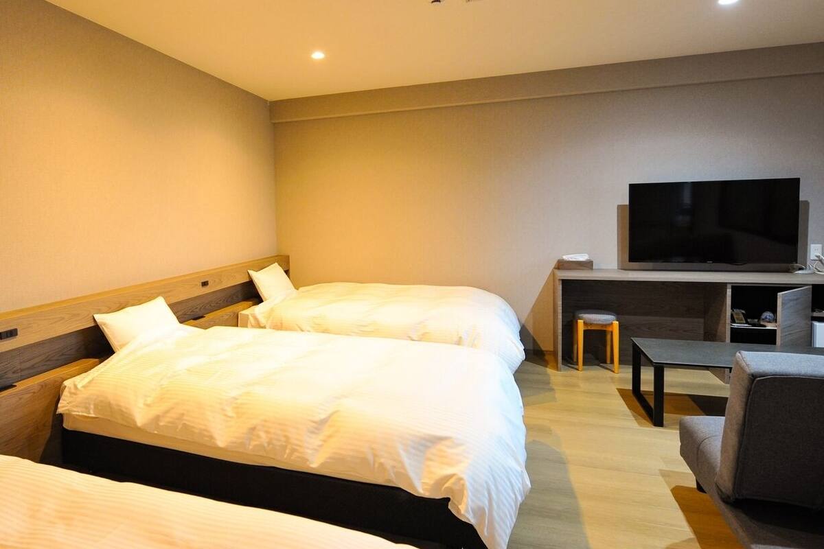 A hotel room with two beds, a TV, a desk, and a chair.