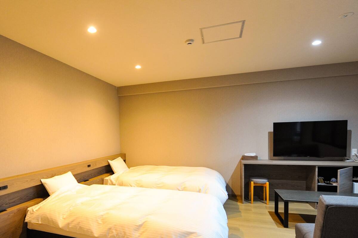 A hotel room with two beds, a TV, a desk, and a chair.