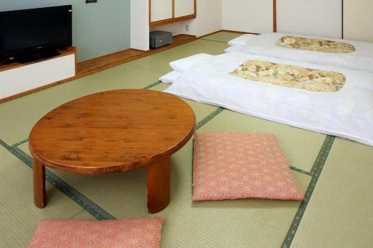 Una habitación tradicional japonesa con suelo de tatami, televisor, mesa de madera y camas futón.