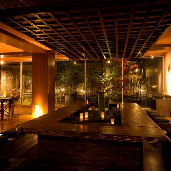 A modern interior with a wooden ceiling, a seating area with cushions, and a view of a garden through glass walls.