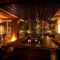 Un interior moderno con techo de madera, un área de descanso con cojines y vistas a un jardín a través de paredes de vidrio.