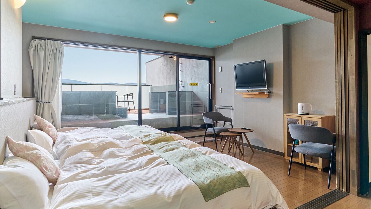 A hotel room with a large bed, a TV, a small table, and a chair.