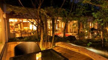 An outdoor patio area with a table and chairs, surrounded by trees and a building with illuminated windows.