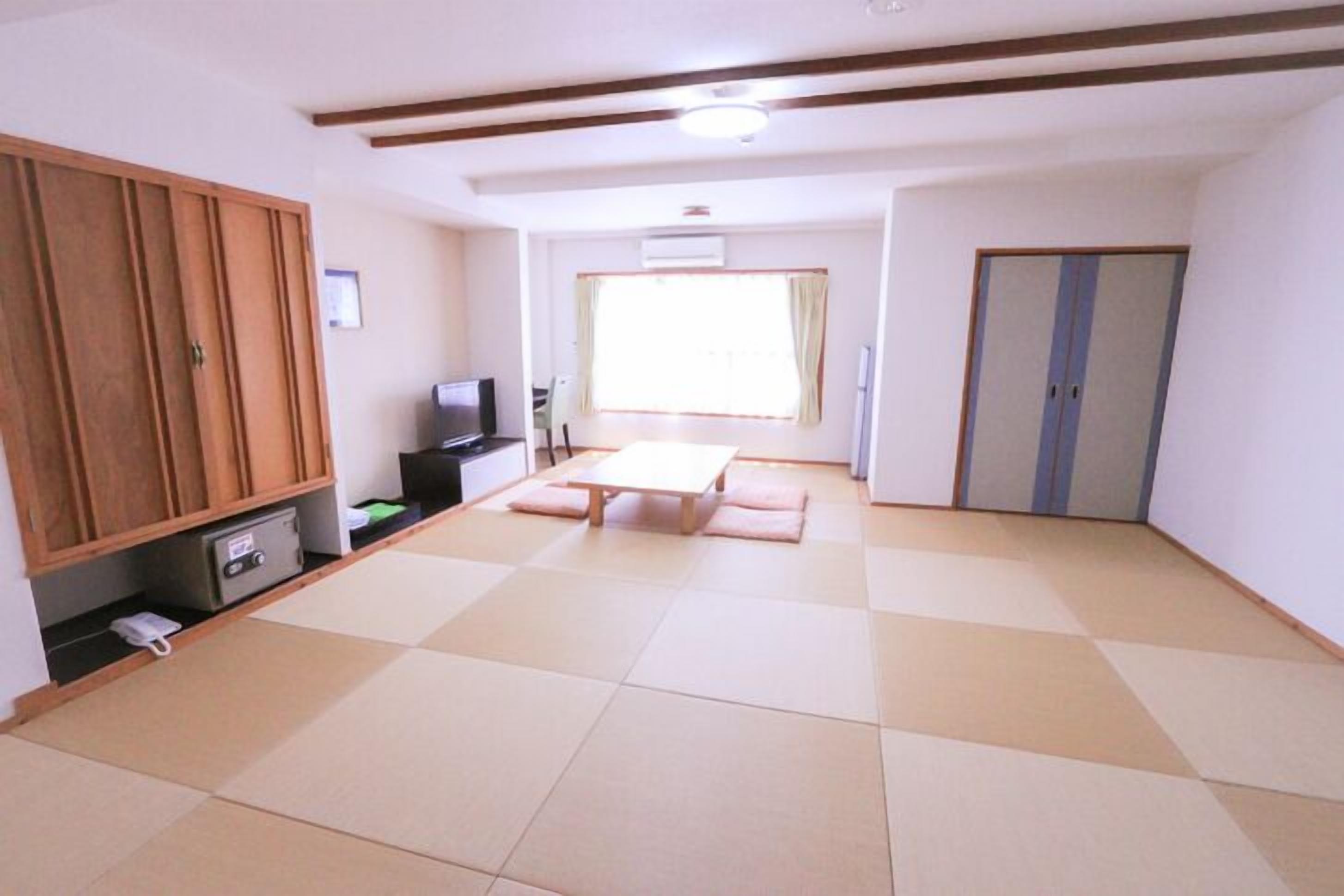 Una habitación con suelo de tatami, un armario de madera, un televisor y una ventana con cortinas.