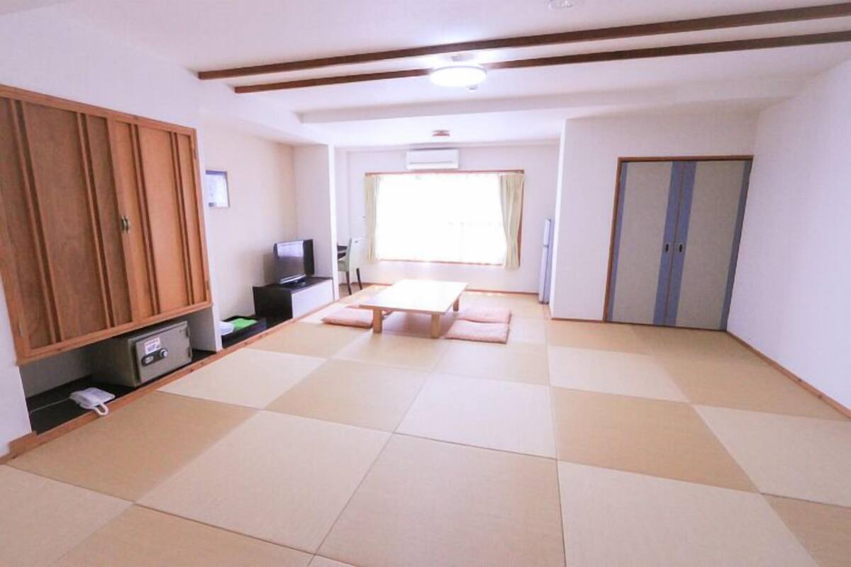 A room with tatami flooring, a wooden wardrobe, a television, and a window with curtains.