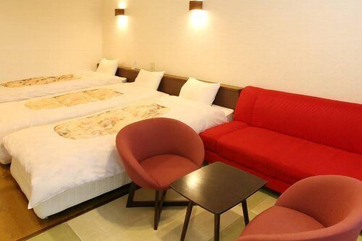 A hotel room with two beds, a red sofa, two red chairs, and a small table.