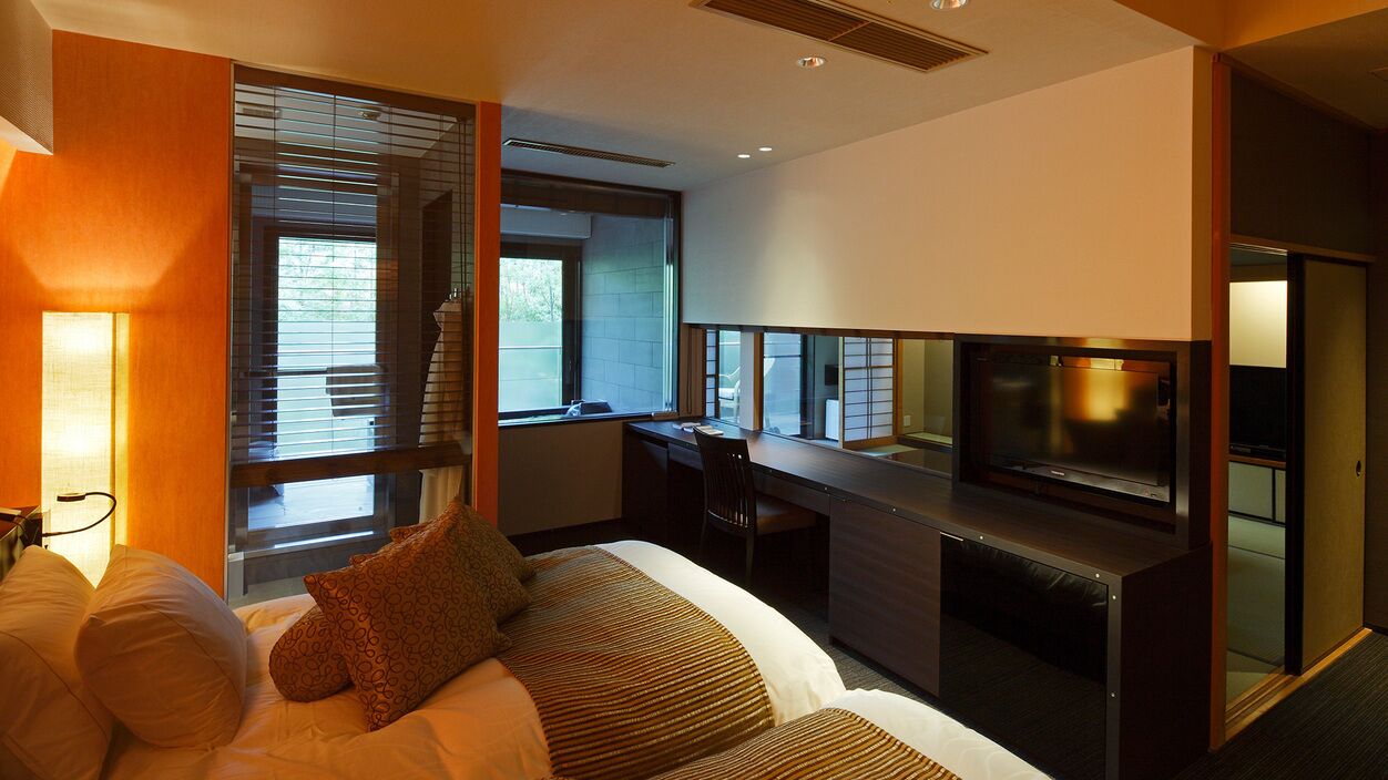 Een hotelkamer met een bed, een bureau, een televisie en een raam met jaloezieën.