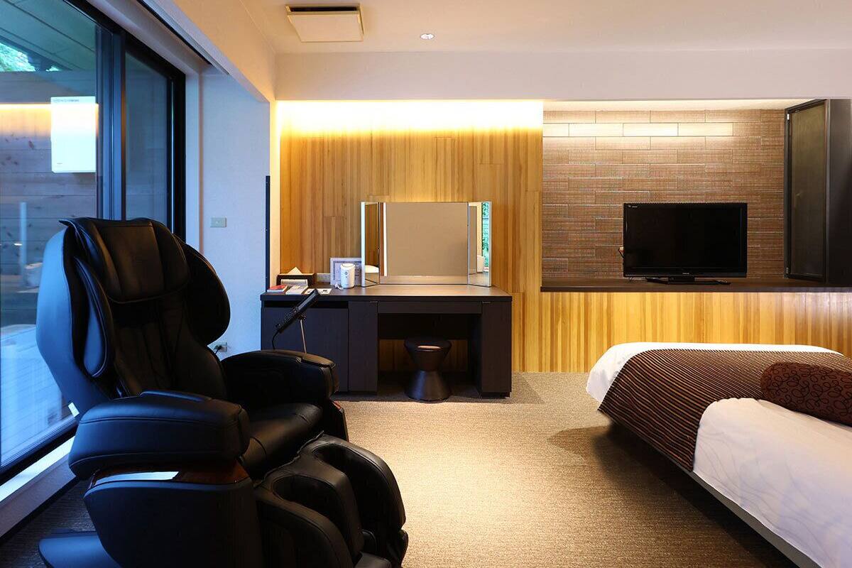Une chambre d’hôtel équipée d’un fauteuil de massage, d’un bureau avec un ordinateur, d’une télévision et d’un lit.