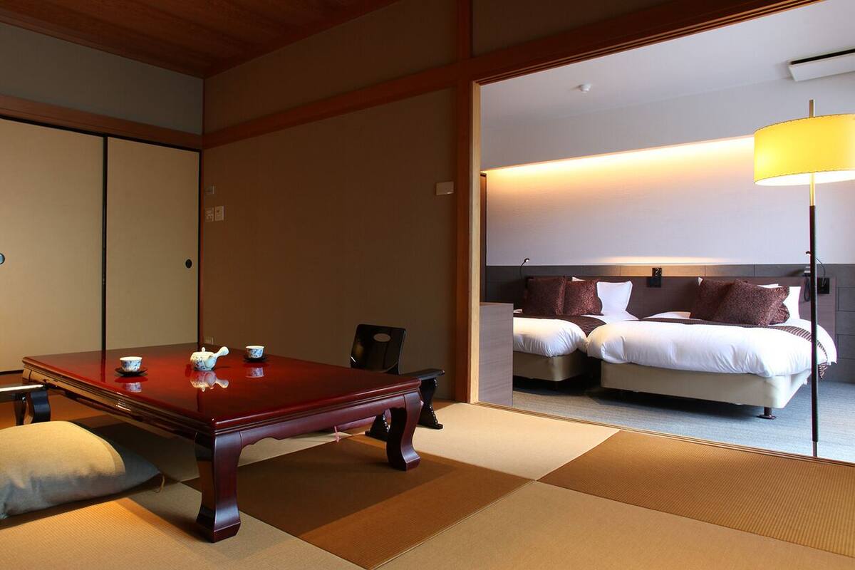 Une pièce de style japonais traditionnel, avec un sol recouvert de tatamis, une petite table en bois et un lit doté d’une tête de lit.