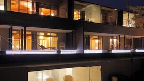 Un bâtiment moderne à plusieurs étages, doté de murs en verre, d’un espace extérieur aménagé avec des sièges et d’un balcon.