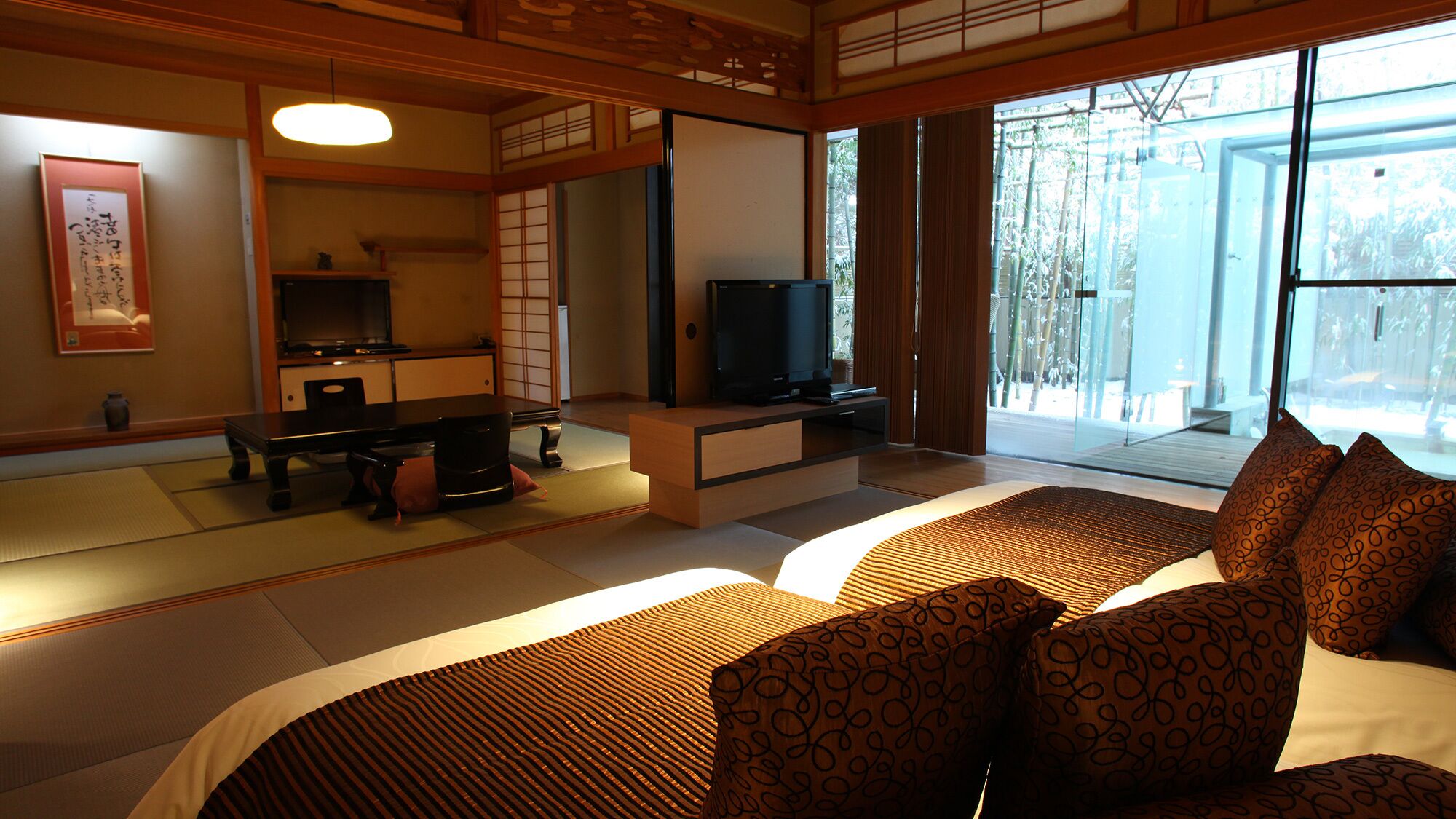 Een traditionele Japanse kamer met tatami vloerbedekking, een lage tafel, een televisie en een bed met gestreepte kussens.