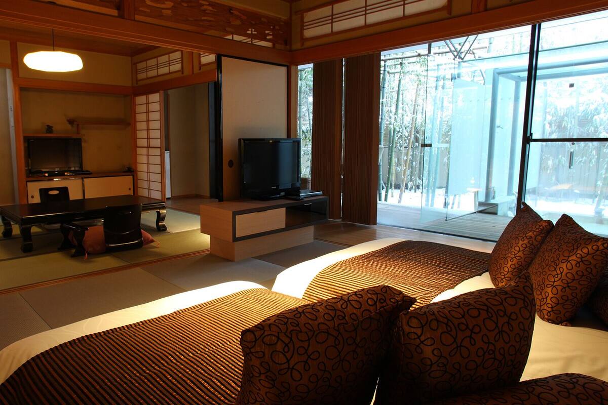 Une pièce de style japonais traditionnel, avec un sol recouvert de tatamis, une table basse, un téléviseur et un lit agrémenté de coussins à motifs.