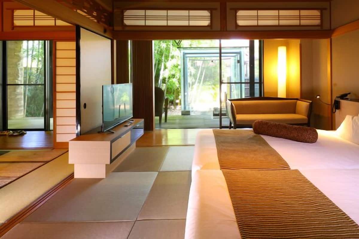 Une chambre d’hôtel avec un grand lit, une télévision, un canapé et une vue sur la verdure environnante.