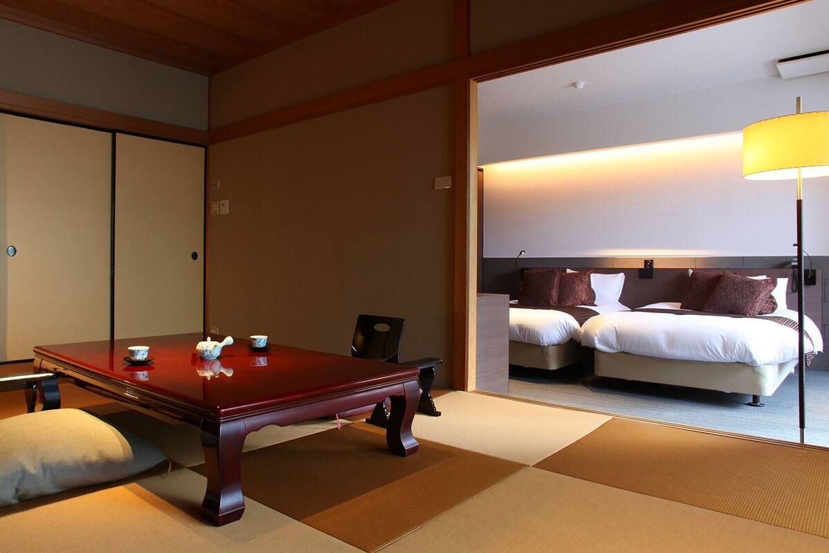 Une pièce de style japonais traditionnel, avec un sol recouvert de tatamis, une basse table en bois, un canapé et un lit doté d’une tête de lit.