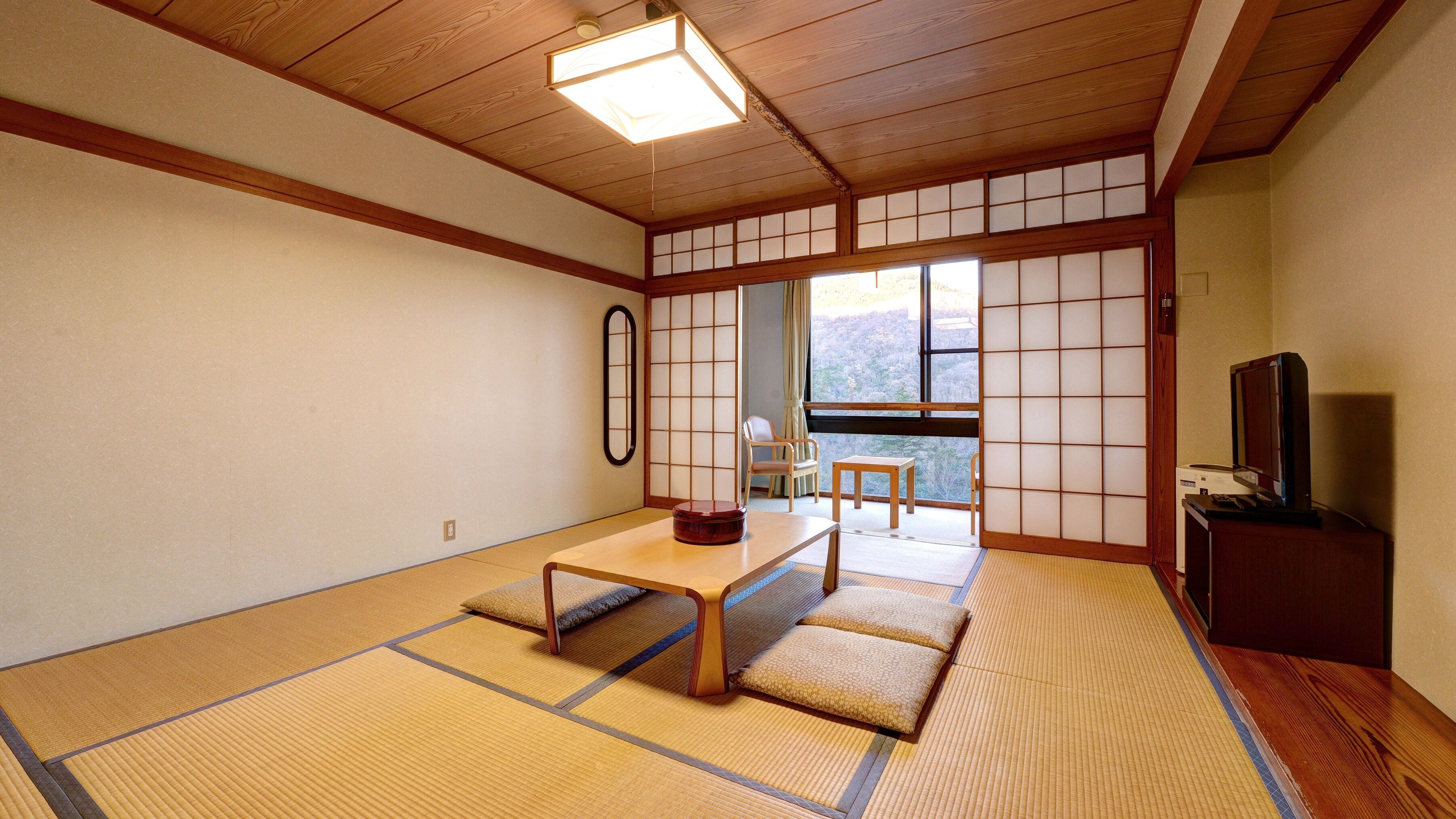Une pièce de style japonais traditionnel, avec un sol recouvert de tatamis, une table basse, un téléviseur et une vue sur l’extérieur.