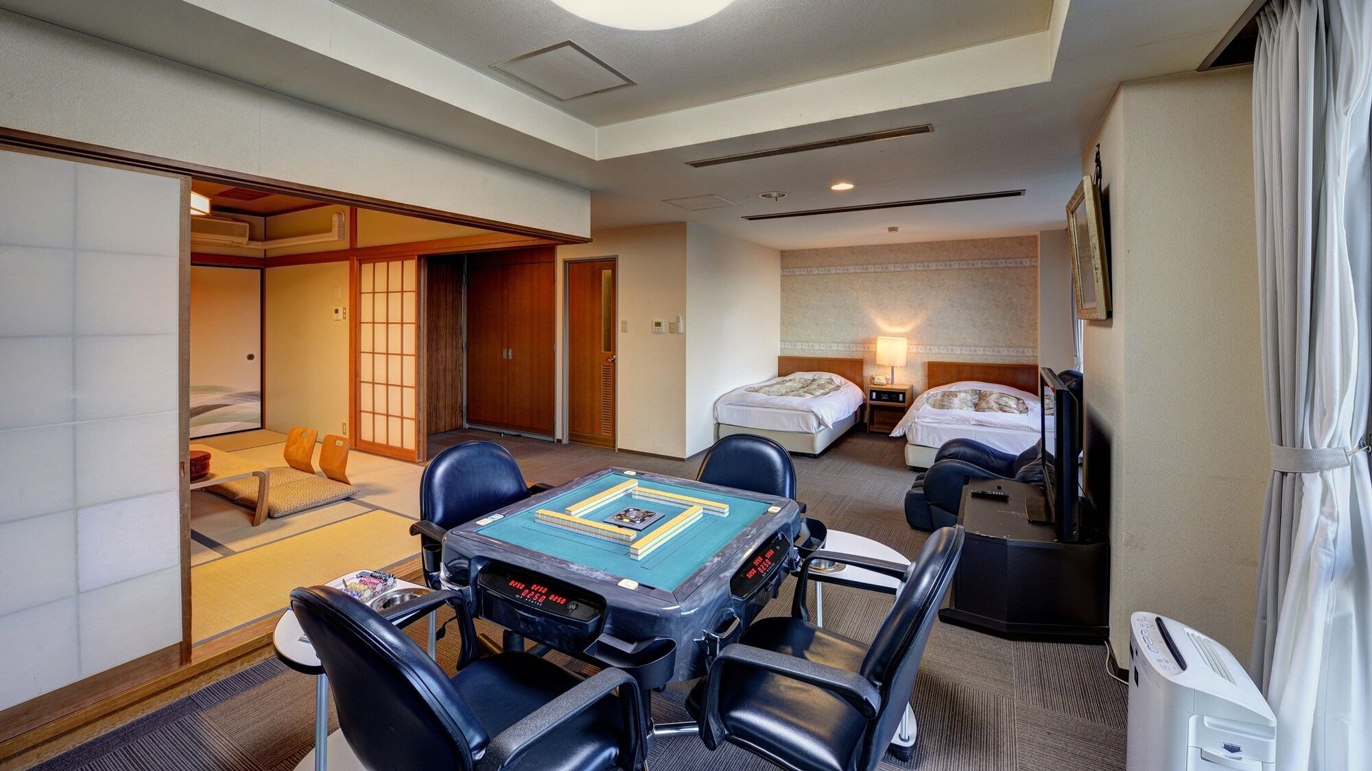 Une chambre d’hôtel comprenant un espace détente avec des tatamis, un lit, un bureau avec un ordinateur et un téléviseur.