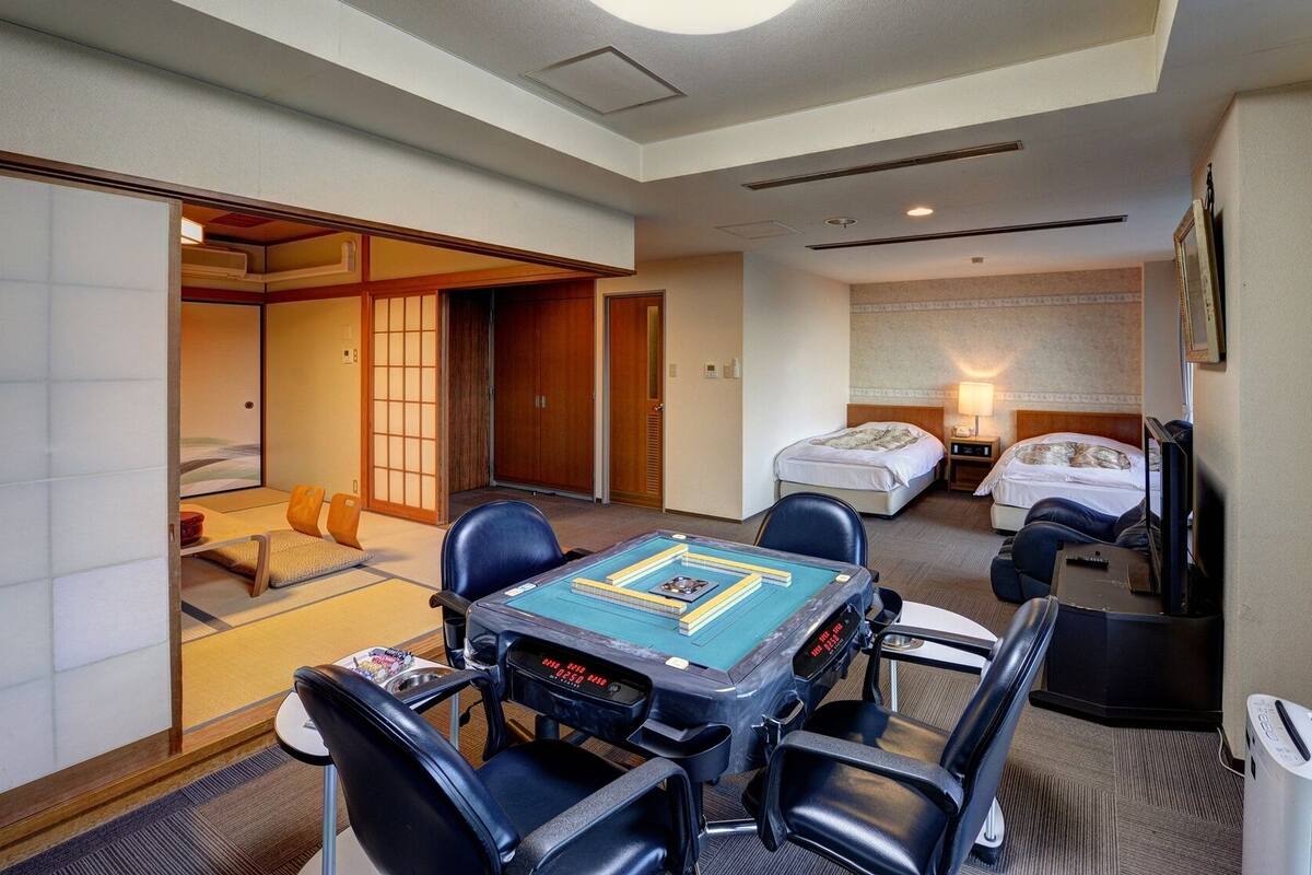 Une chambre d’hôtel comprenant un espace détente avec des tatamis, un lit, un bureau avec un ordinateur et un téléviseur.