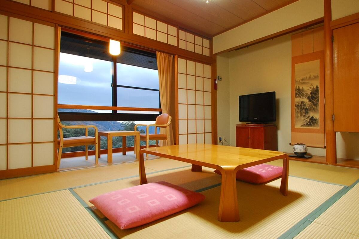 Une pièce de style japonais traditionnel, avec un sol recouvert de tatamis, une petite table en bois, un téléviseur et des portes coulissantes.