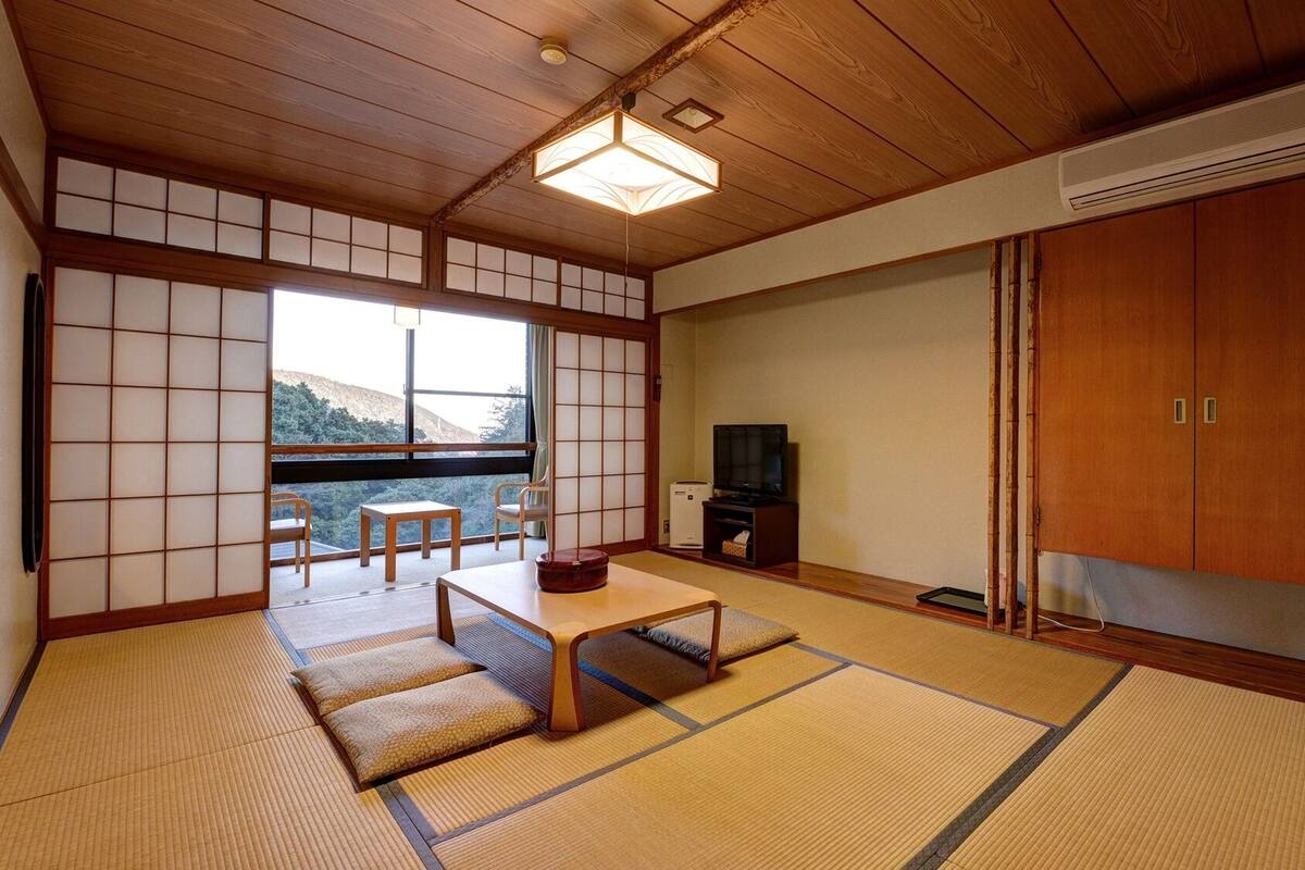 Une pièce de style japonais traditionnel, avec un sol recouvert de tatamis, une petite table basse avec des coussins, un téléviseur et une porte coulissante.