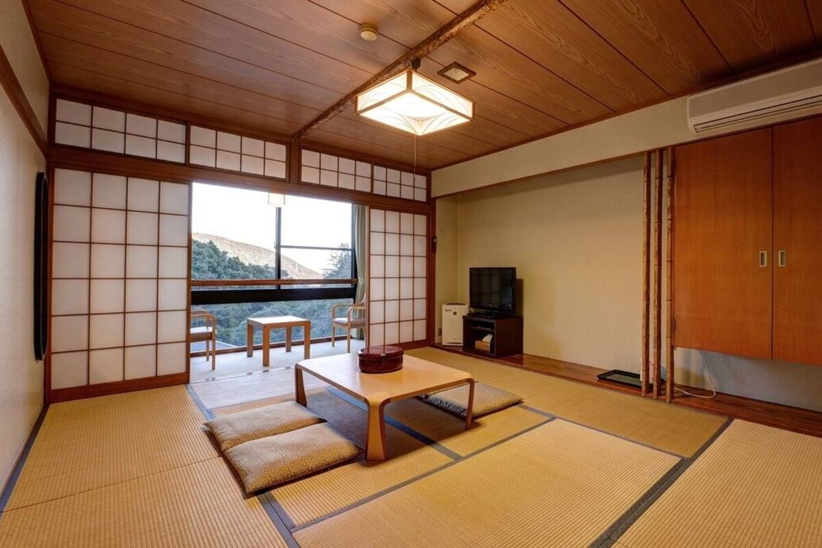 Une pièce de style japonais traditionnel, avec un sol recouvert de tatamis, une petite table basse, un téléviseur et une porte coulissante donnant sur un balcon.