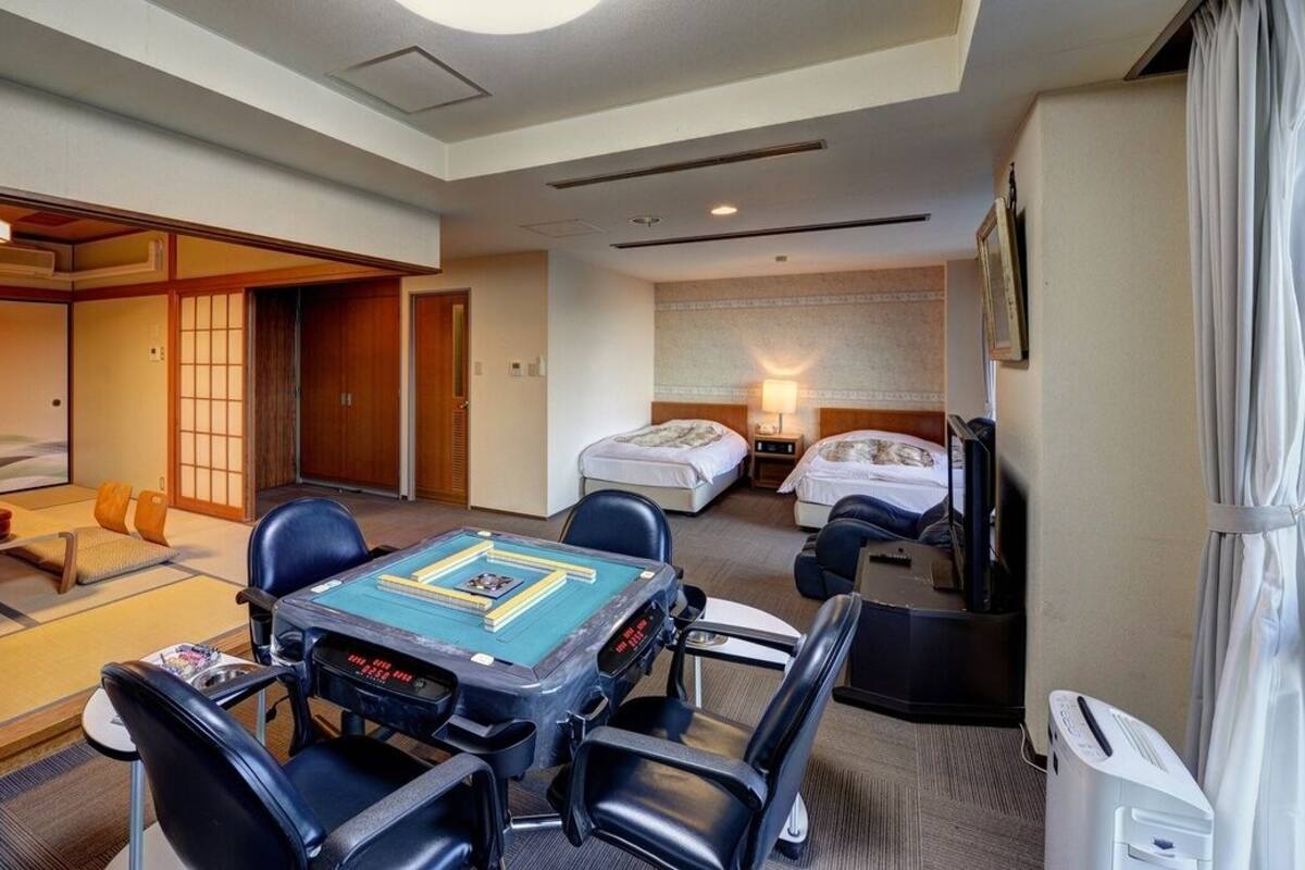 Une chambre d’hôtel avec un espace détente doté de tatamis, un lit avec une tête de lit, une table de chevet avec une lampe et un téléviseur.