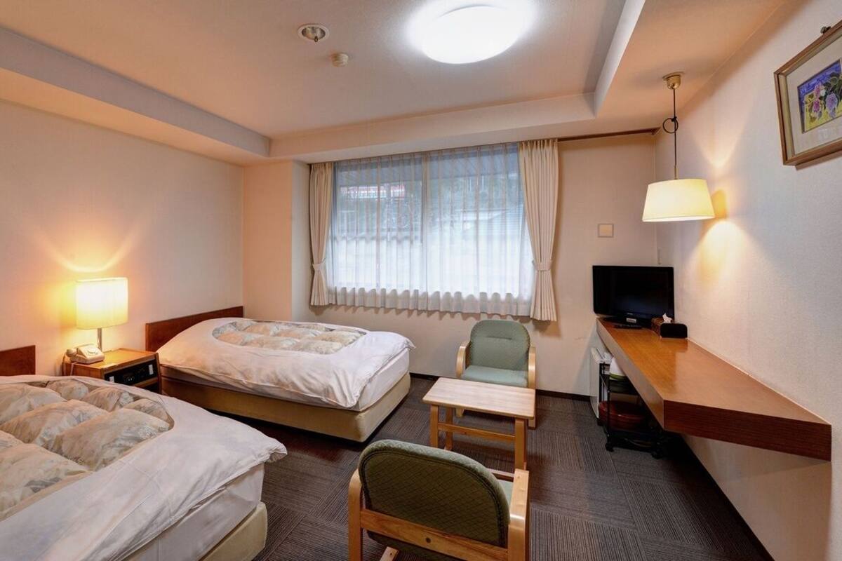 Une chambre d’hôtel avec deux lits, un bureau, une chaise, une télévision et une fenêtre avec des rideaux.