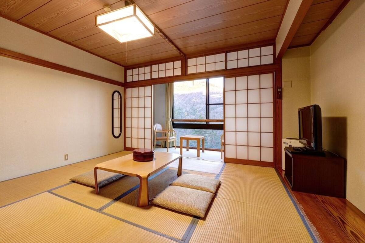 Une pièce de style japonais traditionnel, avec un sol recouvert de tatamis, une table basse, un téléviseur et une vue à travers un paravent en papier.