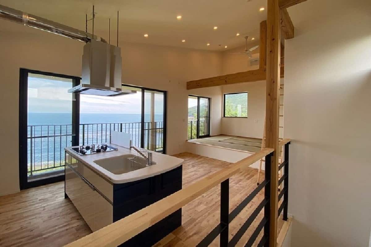 A modern kitchen with a large island, a view of the sea, and a balcony.