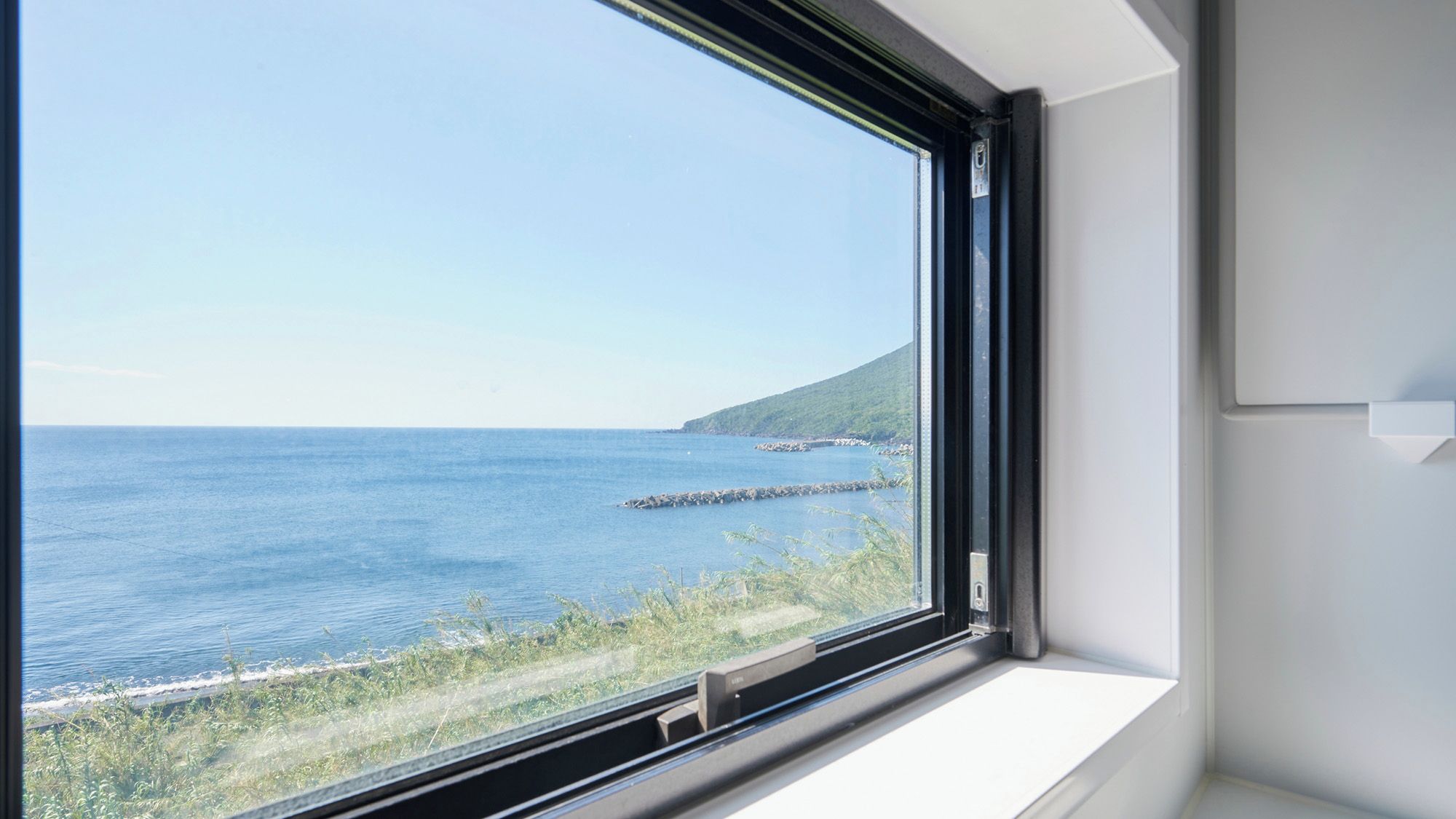 A window with a view of the sea and a rocky coastline.