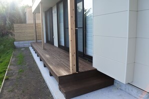 A modern building with a wooden deck, large sliding glass doors, and a white exterior wall. - Kino-saji (Ibusuki)