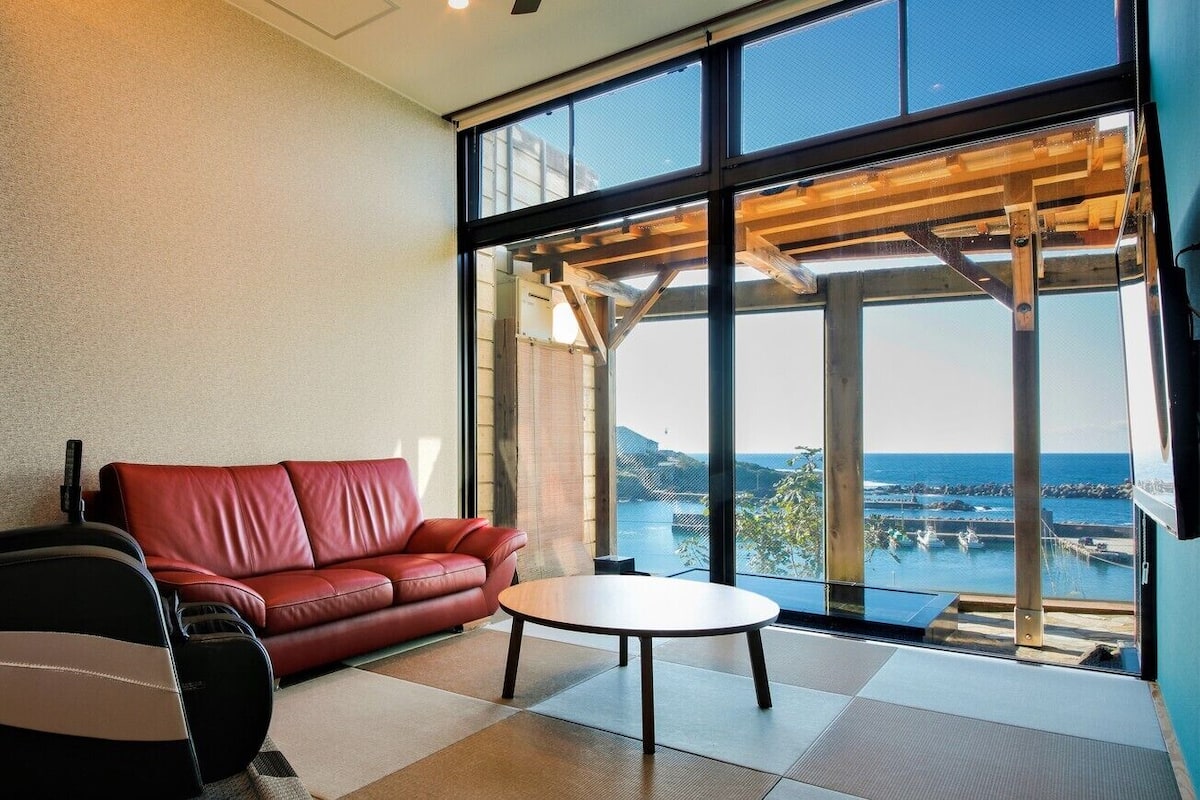 A modern room with a red leather sofa, a small round table, and a large window overlooking a body of water.