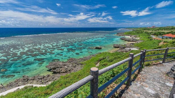 Paisagem costeira com águas azul-turquesa cristalinas, rochedos e uma cerca de madeira.