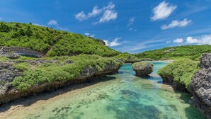 Paisagem costeira com águas turquesa cristalinas, formações rochosas e vegetação exuberante.