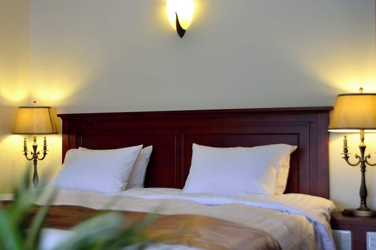A hotel room with a wooden headboard, two bedside lamps, and a wall-mounted light fixture.