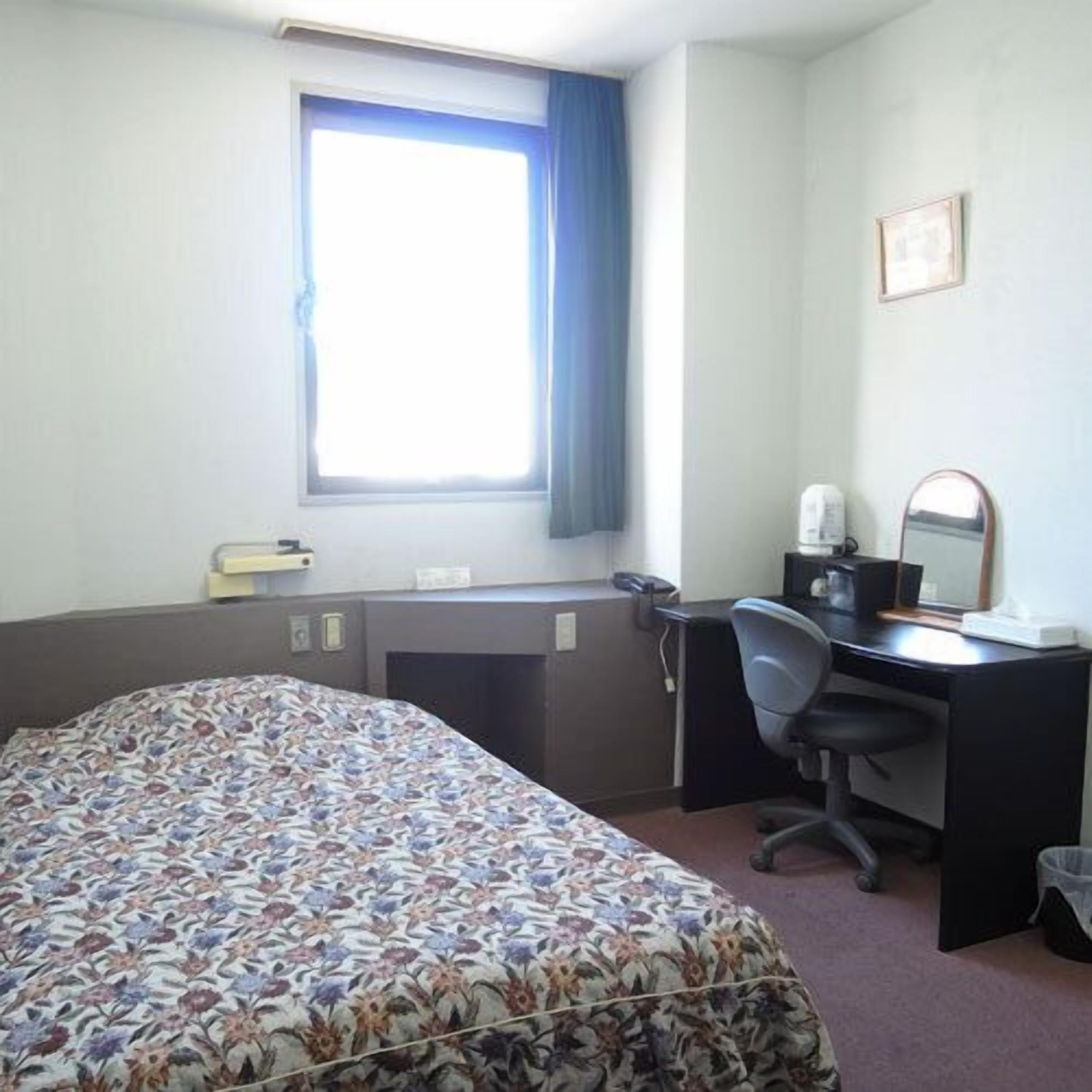 Une chambre d’hôtel avec un lit, un bureau, une chaise et une fenêtre avec des rideaux.